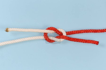 Téléchargez les photos : Rope grief knot, similar to reef knot, but impractical and used as device for trick, view on a blue background - en image libre de droit