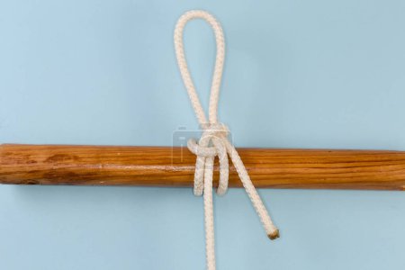 Foto de Rope knot Highwaymans hitch, used as a quick-release draw hitch tied around a wooden pole, view close-up on a blue background - Imagen libre de derechos