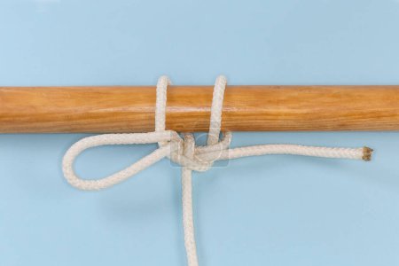 Foto de Nudo de cuerda para bajar un cubo, utilizado para unir una cuerda a un objeto como un enganche de extracción rápida atado alrededor de un poste de madera, ver de cerca sobre un fondo azul - Imagen libre de derechos