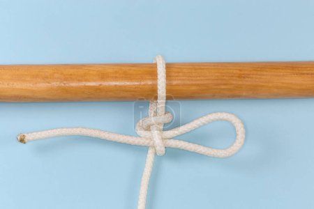 Foto de Nudo de cuerda Enganche de punto alto, utilizado para unir una cuerda a un objeto como un enganche de extracción rápida atado alrededor de un poste de madera, vista de cerca sobre un fondo azul - Imagen libre de derechos