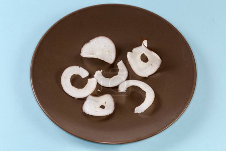 Foto de Los trozos secos de la carne de coco en forma de los círculos sobre el plato castaño oscuro sobre el fondo azul - Imagen libre de derechos