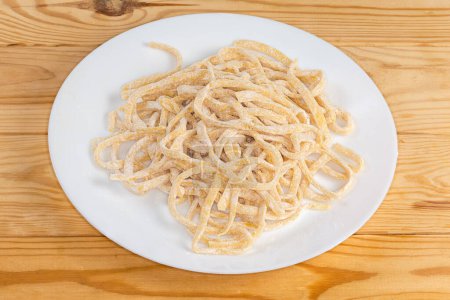 Raw homemade egg noodles in the shape of the long strips on a white dish on rustic table