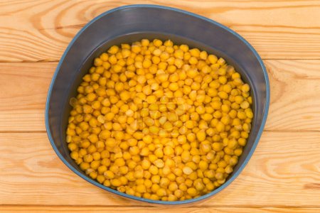 Téléchargez les photos : Pois chiches jaunes entiers non cuits trempés dans l'eau froide dans le bol bleu-gris avant de se préparer à une cuisson plus rapide sur la table rustique, vue du dessus - en image libre de droit