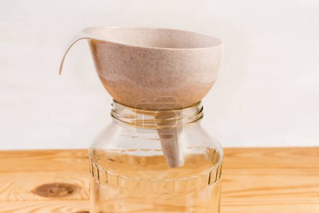 Plastic kitchen funnel for pouring liquids and powders on the mouth of empty glass jar on a rustic table, side view