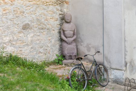 Foto de Piedra áspera hembra kurgan obelisco de pie junto a la antigua muralla de la fortaleza con una antigua bicicleta de mujer moderna en un primer plano - Imagen libre de derechos