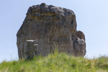 Foto de Antigua cruz de piedra entre la hierba en la tumba cosaca medieval en la colina contra la gran roca arenisca en un día soleado - Imagen libre de derechos