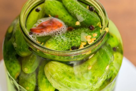 Photo for Naturally fermented quick pickled cucumbers in jar during souring, view through the jar neck close-up in selective focus - Royalty Free Image