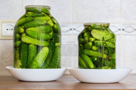 Photo for Naturally fermented quick pickled cucumbers in two jars of different sizes during souring on a kitchen table, side view - Royalty Free Image