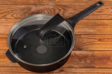 Photo for Empty deep frying pan made of cast aluminum with titanium non-stick coating closed with lid of glass and stainless steel on the rustic table - Royalty Free Image