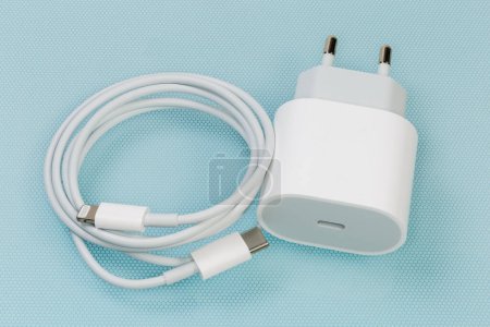 Foto de Cargador blanco con toma de salida USB Tipo-C para la carga de baterías de accesorios electrónicos portátiles y cable adecuado, primer plano en la superficie azul - Imagen libre de derechos
