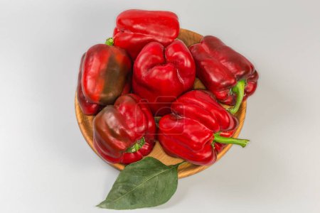 Photo for Several whole freshly harvested red bell peppers and leaf of the pepper plant on the wooden dish on a grey background - Royalty Free Image