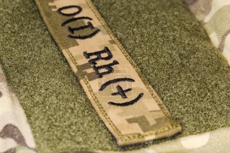 Foto de Pegatina militar con designación de tipo sanguíneo "O (I) RH +" y cierre textil sobre un uniforme de camuflaje, primer plano en enfoque selectivo - Imagen libre de derechos