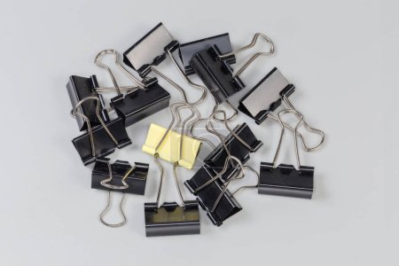 Photo for Small heap of the black binder clips for paper and one the same yellow binder among them on a gray surface - Royalty Free Image