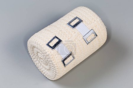Foto de Venda médica elástica tejida moderna con clips estirables de aluminio enrollados en rollo sobre un fondo gris - Imagen libre de derechos