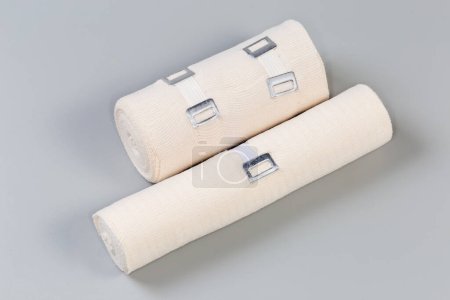 Foto de Dos vendas médicas elásticas tejidas modernas diferentes tamaños con clips estirables de aluminio enrollados en rollos sobre un fondo gris - Imagen libre de derechos