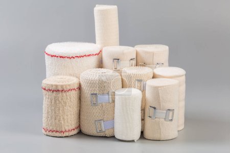 Photo for Set of modern woven elastic medical bandages different sizes rolled into rolls, some of them with aluminum stretchable clips stand on a gray surface, side view close-up - Royalty Free Image