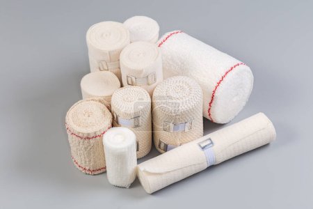 Photo for Set of the modern woven elastic medical bandages different sizes rolled into rolls, some of them with aluminum stretchable clips on a gray surface - Royalty Free Image