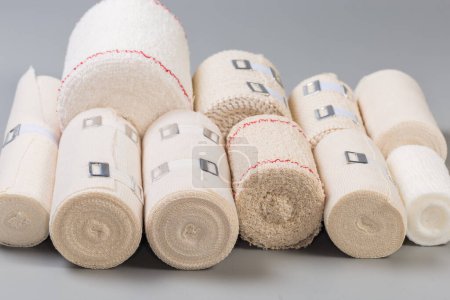 Photo for Set of modern woven elastic medical bandages different sizes rolled into rolls, some of them with aluminum stretchable clips lie on a gray surface, side view close-up in selective focus - Royalty Free Image