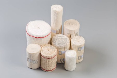 Photo for Set of modern woven elastic medical bandages different sizes rolled into rolls, some of them with aluminum stretchable clips on a gray background - Royalty Free Image