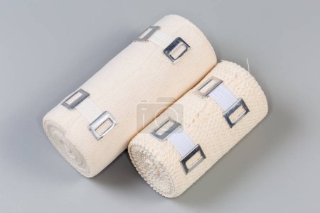 Foto de Dos vendas médicas elásticas tejidas modernas diferentes tamaños y estructura de tela con clips estirables de aluminio enrollados en rollos sobre un fondo gris - Imagen libre de derechos