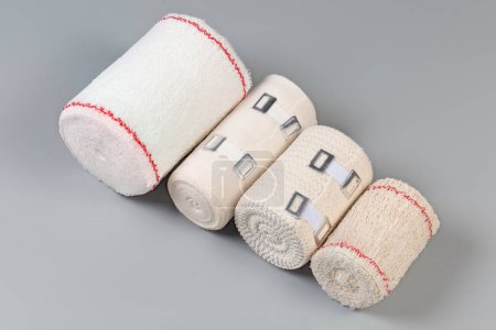 Photo for Several modern woven elastic medical bandages different sizes and fabric structure, some of them with aluminum stretchable clips rolled into rolls on a gray background - Royalty Free Image