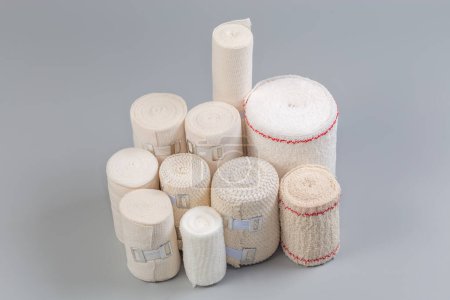 Photo for Set of modern woven elastic medical bandages different sizes and fabric structure rolled into rolls, some of them with aluminum stretchable clips on a gray background - Royalty Free Image