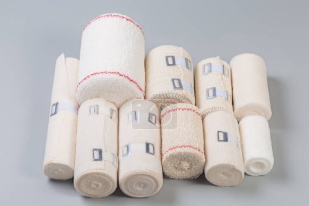 Photo for Set of modern woven elastic medical bandages different sizes and fabric structure rolled into rolls, some of them with aluminum stretchable clips on a gray background - Royalty Free Image