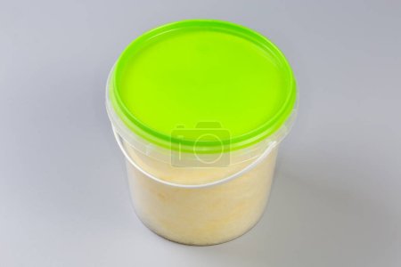 Photo for Banana-flavored cotton candy thicker consistency in the plastic container closed with green lid on a gray background - Royalty Free Image