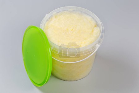 Photo for Banana-flavored cotton candy of thick consistency in the plastic container with removed green lid on a gray background - Royalty Free Image