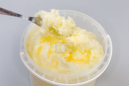 Photo for Banana-flavored cotton candy of thick consistency in the open plastic container with dessert fork on a gray background - Royalty Free Image