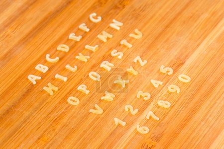 Foto de Pasta cruda en forma de letras mayúsculas del alfabeto inglés y números arábigos colocados en filas en el orden alfabético en la tabla de cortar, vista lateral de cerca en enfoque selectivo - Imagen libre de derechos