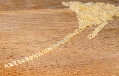 Foto de Pasta cruda en forma de letras mayúsculas del alfabeto inglés y números arábigos colocados en líneas en el orden alfabético que se extiende desde un montón en la tabla de cortar, enfoque selectivo - Imagen libre de derechos