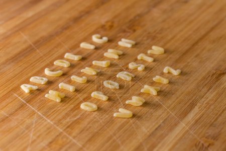 Foto de Pastas crudas en forma de letras mayúsculas del alfabeto inglés colocadas en filas en orden alfabético en la tabla de cortar de bambú, primer plano en enfoque selectivo - Imagen libre de derechos