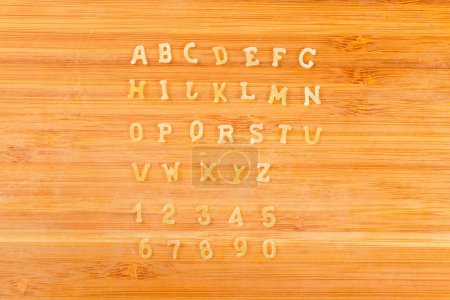 Foto de Pasta cruda en forma de letras mayúsculas del alfabeto inglés y números arábigos colocados en filas en el orden alfabético en la tabla de cortar, vista superior de cerca - Imagen libre de derechos