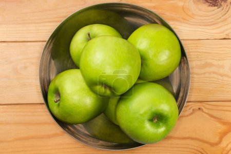 Photo for Whole green apples in the stainless steel kitchen bowl, top view on a rustic table - Royalty Free Image