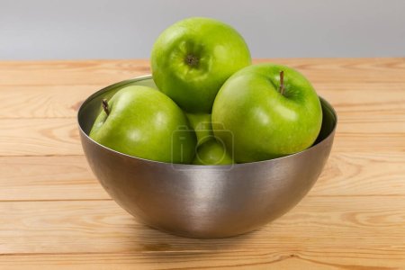 Photo for Whole green apples in the stainless steel kitchen bowl, side view on a rustic table - Royalty Free Image