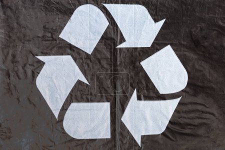Photo for White universal recycling symbol on the black slightly wrinkled food plastic bag made from the recycled plastic, close-up - Royalty Free Image
