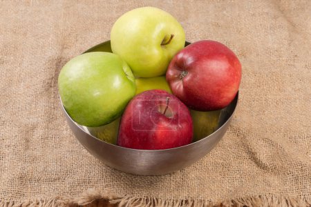 Photo for Whole green, yellow and red apples in the stainless steel kitchen bowl on a surface covered with sackcloth - Royalty Free Image