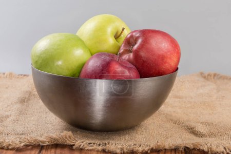Photo for Whole green, yellow and red apples in the stainless steel kitchen bowl on a surface covered with sackcloth, side view - Royalty Free Image