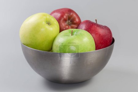 Photo for Whole green, yellow and red apples in the stainless steel kitchen bowl on a gray background, side view - Royalty Free Image