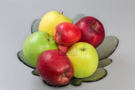 Photo for Whole green, yellow and red apples on the glass fruit bowl on a gray background - Royalty Free Image