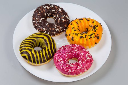 American-style ring shaped doughnuts with different filling, glazes and sprinkles on a white dish on a gray background