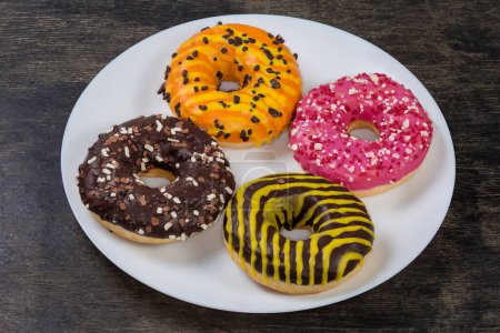 American-style ring shaped doughnuts with different filling, glazes and sprinkles on a white dish on a black surface