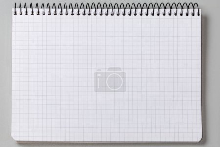 Foto de Hoja en blanco de papel cuadrado de un libro de ejercicios escolares o cuaderno de papel con encuadernación en espiral de alambre negro sobre un fondo gris, vista superior - Imagen libre de derechos
