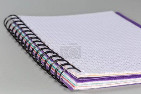 Foto de Libro de ejercicios de escuela abierta, o cuaderno de papel con hojas en blanco de papel cuadrado y encuadernación en espiral de alambre negro sobre un fondo gris, vista lateral en enfoque selectivo - Imagen libre de derechos