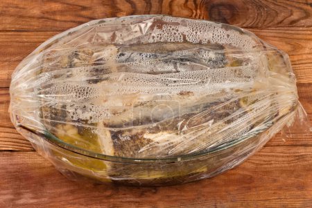 Pieces of hake baked in the glass casserole pan placed in the plastic heatproof oven bag for juicy healthy baking on the old rustic table