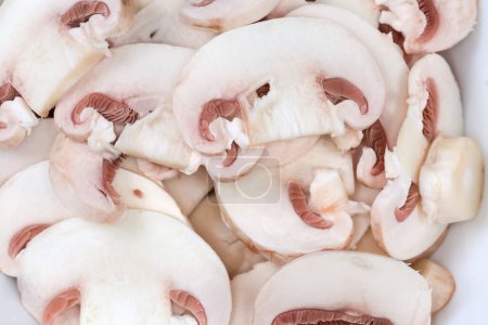 Background of the fresh uncooked button mushrooms chopped into thin slices, top view close-up