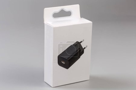 Closed rectangular hang tab packing box made with light cardboard for USB charger with AC Euro plug on a gray surface