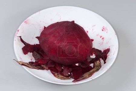Whole raw round red beetroot peeled from the skin among the peelings in bowl on a gray background
