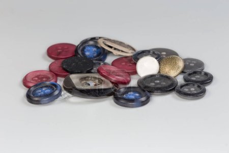Photo for Small heap of modern plastic, metal and fabric-covered flat sew-through and shank buttons of different design, side view on a gray background close-up in selective focus - Royalty Free Image